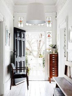 an entryway with white walls and stained glass windows, wooden furniture, and a bench