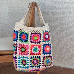 a multicolored crocheted bag sitting on top of a wooden chair next to a white wall