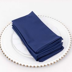 a stack of blue napkins sitting on top of a white plate with gold beaded trim