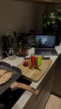 a laptop computer sitting on top of a counter next to a cutting board with vegetables