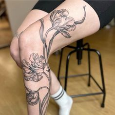 a woman sitting on top of a wooden floor next to a chair with flowers tattooed on her legs