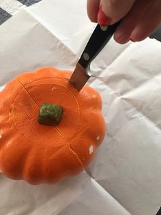 a person is cutting into a small pumpkin with a sharp knife on top of it