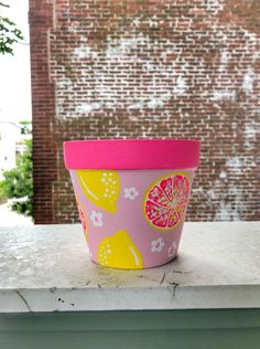 a pink and yellow flower pot sitting on top of a white table next to a brick wall