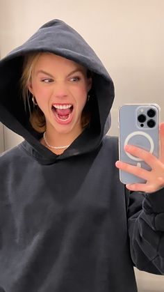 a woman in a hoodie holding up a cell phone