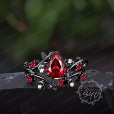 a ring with red stones and silver accents on top of a black stone slab in front of a green leafy background