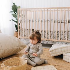 a baby sitting on the floor in front of a crib