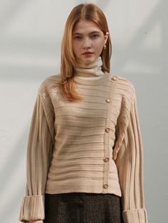 a woman wearing a beige sweater and black skirt standing in front of a white wall