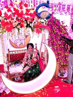 a woman sitting on top of a crescent shaped bench next to flowers and other decorations