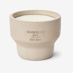 a white candle sitting inside of a cement cup on a table top with the words, resfields nyc etched in it