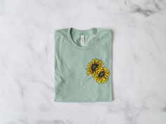 Sunflower T-Shirt *Product Details - Unisex T-Shirt - Ultra soft Bella Canvas 3001 - Designed with high quality pre-shrunk combed and ring-spun cotton - Features a crew neck with shoulder to shoulder taping and side seams *Sizing and Colors - Please refer to sizing and color charts in the images *Fabrication - Solid colors: 100% combed and ring-spun cotton - Heather colors: 52% combed and ring-spun cotton, 48% polyester - Athletic Heather colors: 90% combed and ring-spun cotton, 10% polyester - Cotton Crew Neck T-shirt With Sunflower Design, Casual Green Sunflower Print Top, Green Cotton Sunflower Print Top, Green Cotton Top With Sunflower Print, Spring Green T-shirt With Custom Print, Cotton T-shirt With Sunflower Design, Casual Sunflower Design T-shirt With Relaxed Fit, Relaxed Fit Short Sleeve T-shirt With Sunflower Design, Casual Sunflower Design T-shirt In Relaxed Fit