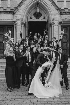 a bride and groom kissing in front of a church with their wedding party waving at the camera