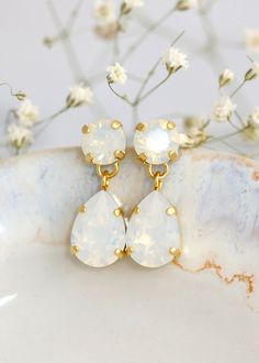 two white earrings sitting on top of a marble slab with flowers in the back ground