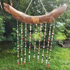 a wooden branch with beads hanging from it's side in the grass next to some trees