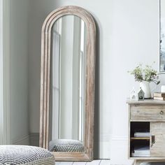 a mirror sitting on top of a wooden dresser next to a white wall and floor