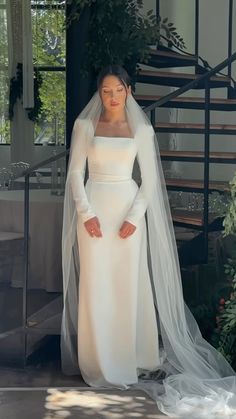 a woman wearing a white wedding dress and veil standing in front of a set of stairs