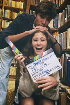 a man and woman holding a clapper in front of bookshelves