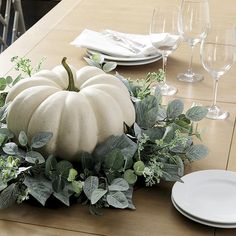 a white pumpkin sitting on top of a wooden table next to plates and wine glasses