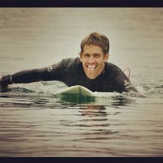 a man riding on top of a surfboard in the ocean with his tongue out