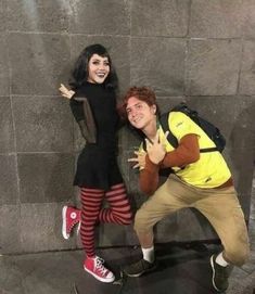 two people posing for a photo in front of a stone wall with one person making the peace sign