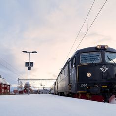 a black train traveling down tracks next to snow covered ground and power lines in the background