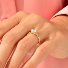 a woman's hand wearing a gold ring with a white diamond on the middle