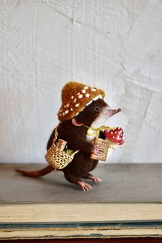 a toy rat with a hat and some food in it's mouth sitting on top of a book