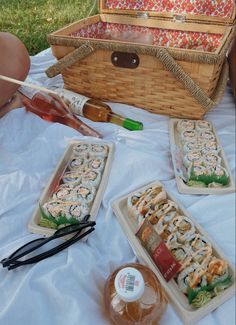 some food is laying out on a blanket near a picnic basket and glass bottle with liquid in it