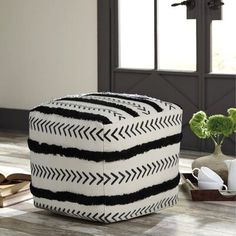 a black and white ottoman sitting on top of a wooden floor next to a vase