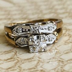 two gold rings with diamonds on them sitting on top of a cloth covered tablecloth