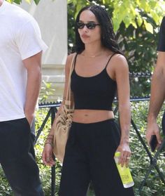 a woman in black pants and crop top walking down the street with a man behind her