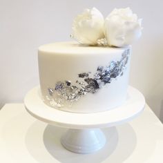 there is a white cake with silver decorations on the top and bottom, sitting on a pedestal