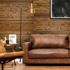 a brown leather couch sitting in front of a wooden wall next to a chair and table