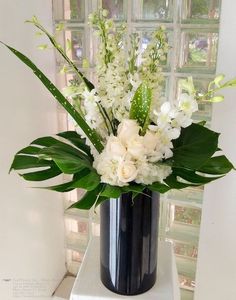 a black vase filled with white flowers and greenery