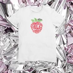 Rock out with this limited edition Beatles t-shirt featuring a graphic print of the iconic Strawberry Fields Forever song. This unisex shirt is made from breathable, machine washable airlume combed and ring spun cotton with a crew neckline and short sleeves. Available in sizes S, M, L, XL, 2XL and 3XL this regular fit shirt is perfect for any music lover looking to add a touch of retro style to their wardrobe. The white cotton fabric is accented with The Beatles Strawberry Fields logo and is a h Fan Merchandise T-shirt For Music Festivals, Sublimation Print Short Sleeve T-shirt For Music Festivals, Graphic Tee With Logo Print For Fan Merchandise, Graphic Tee Shirt With Logo Print For Fans, Short Sleeve Tops For Music Festivals, Summer Fan Apparel Shirt With Screen Print, Band Merch Shirt With Logo Print, Short Sleeve T-shirt For Music Festivals Fan Merchandise, Fan Merchandise Crew Neck Shirt For Music Festivals