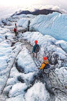 three people climbing up the side of a snow covered mountain