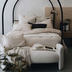 a bed with white linens and pillows in a room next to a brick wall