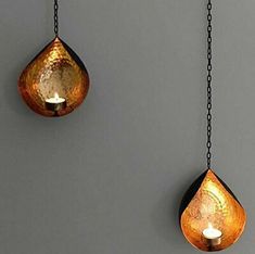 two hanging lights that are made out of copper leaf shapes, one is lit and the other has a candle in it