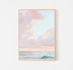 a painting hanging on the wall next to a white wall with a pink and blue sky