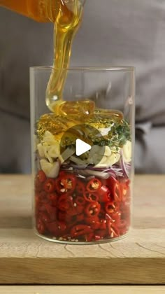 someone pouring olives into a glass filled with vegetables