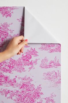 a person's hand on top of a pink and white wallpaper with an envelope