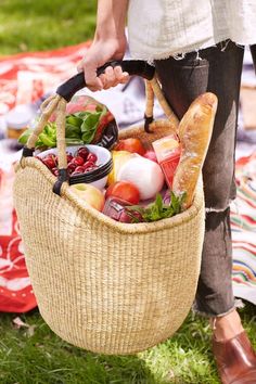 a woman holding a basket full of food on top of a grass covered park area