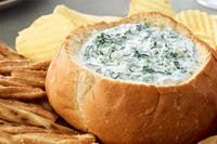 a bread bowl filled with spinach dip surrounded by chips