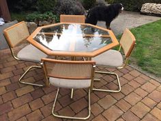 a glass table with four chairs and a black dog in the background