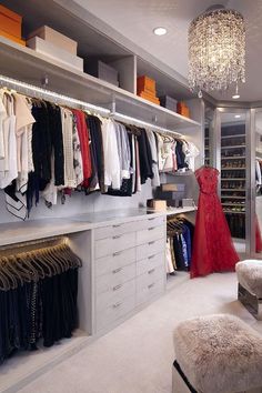 a walk in closet with lots of clothes hanging on the wall and a chandelier