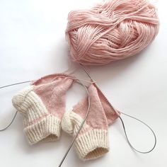 two knitted mittens are sitting next to each other on a white surface, with yarn in the background