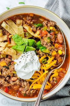 a white bowl filled with taco soup and tortilla chips on the side