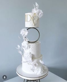 a three tiered wedding cake with white flowers and initials on the top, sitting on a stand