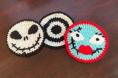 three crocheted coasters with faces on them sitting on a wooden table next to each other