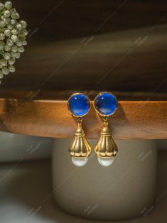 These elegant pearl drop earrings feature a timeless combination of pearl and elegant design. The vibrant blue cabochon stones are set in a delicate gold-toned drop design, and each earring is adorned with a shimmering pearl. The classic style of these earrings makes them a versatile accessory that can be worn with a variety of outfits, from casual to formal. Material: Synthetic Pearl, Resin, Gold-Plated Measurement: 1.5in Every purchase comes with a luxurious velvet pouch, a versatile accessory Classic Blue Pearl Drop Earrings, Elegant Blue Cabochon Clip-on Earrings, Elegant Blue Cabochon Earrings, Pearl Resin, Drop Design, Tigers Eye Gemstone, Tiger Eye Stone, Velvet Pouch, Klein Blue