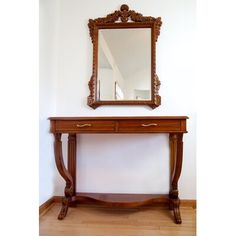 a wooden table with a mirror on top of it next to a white wall and hardwood floor